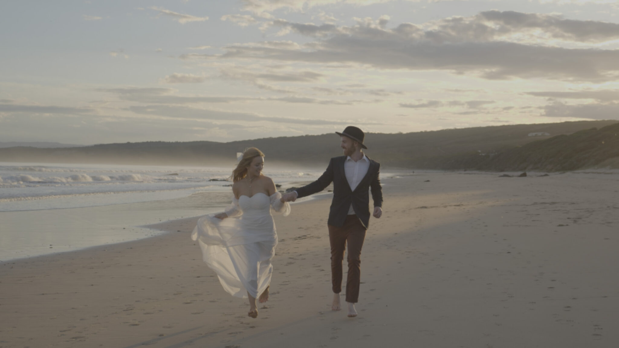 a couple have fun running on a sorrento beach in their wedding film