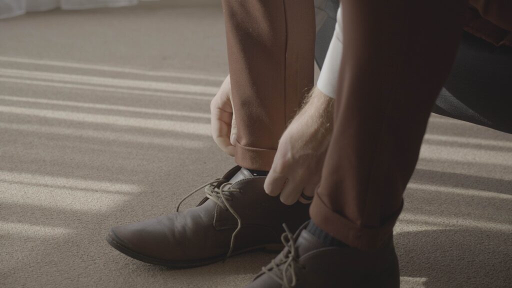 a groom laces up his shoes during his wedding video